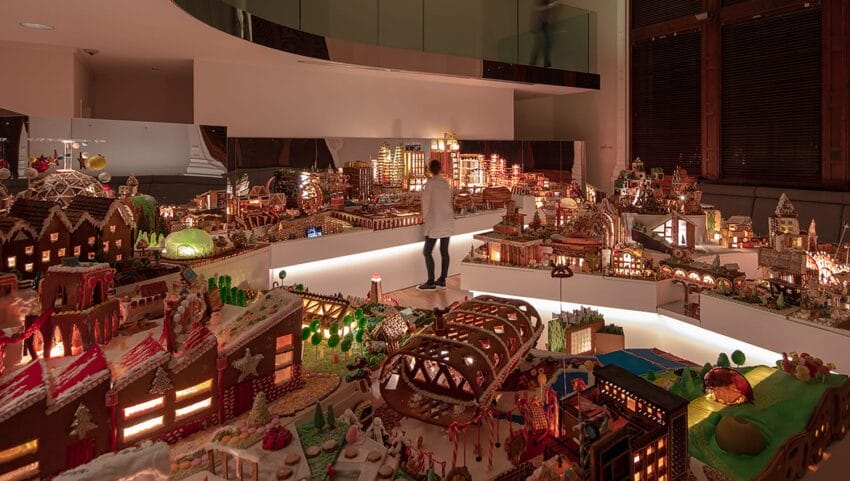 Person exploring an elaborate gingerbread village display with illuminated buildings and intricate details.