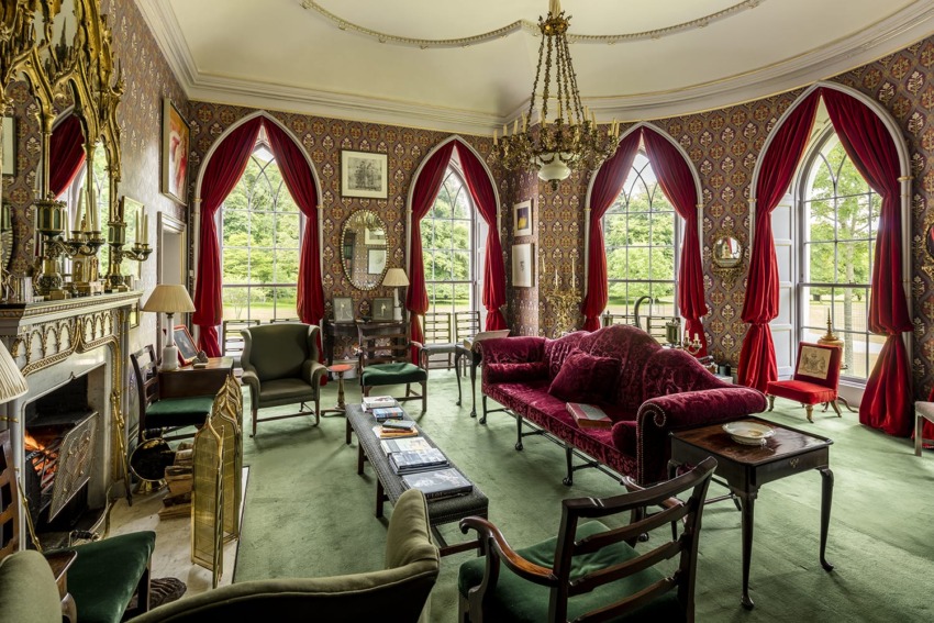 Elegant Victorian-style living room with ornate furniture, red curtains, and lush green carpeting, featuring large windows.