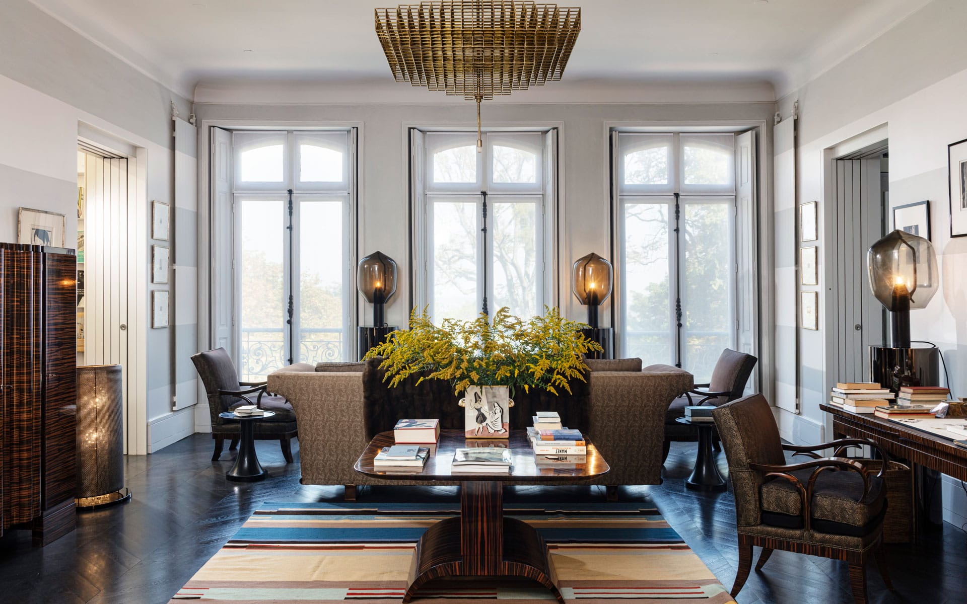 Elegant living room with large windows, stylish furniture, a central wooden table, and a vibrant rug.