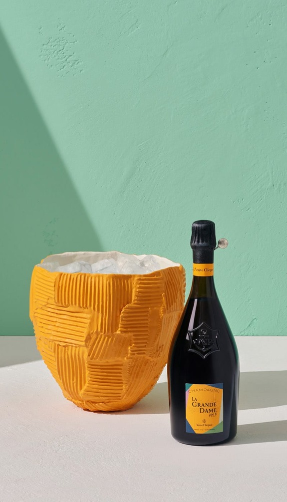 Champagne bottle next to a textured orange vase against a mint green wall.