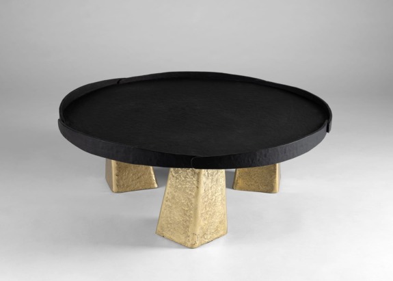 Round black coffee table with gold textured legs on a gray background.