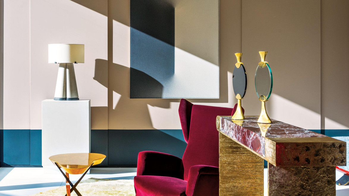 Modern living room with red armchair, marble side table, gold candlesticks, and contemporary art on the wall.