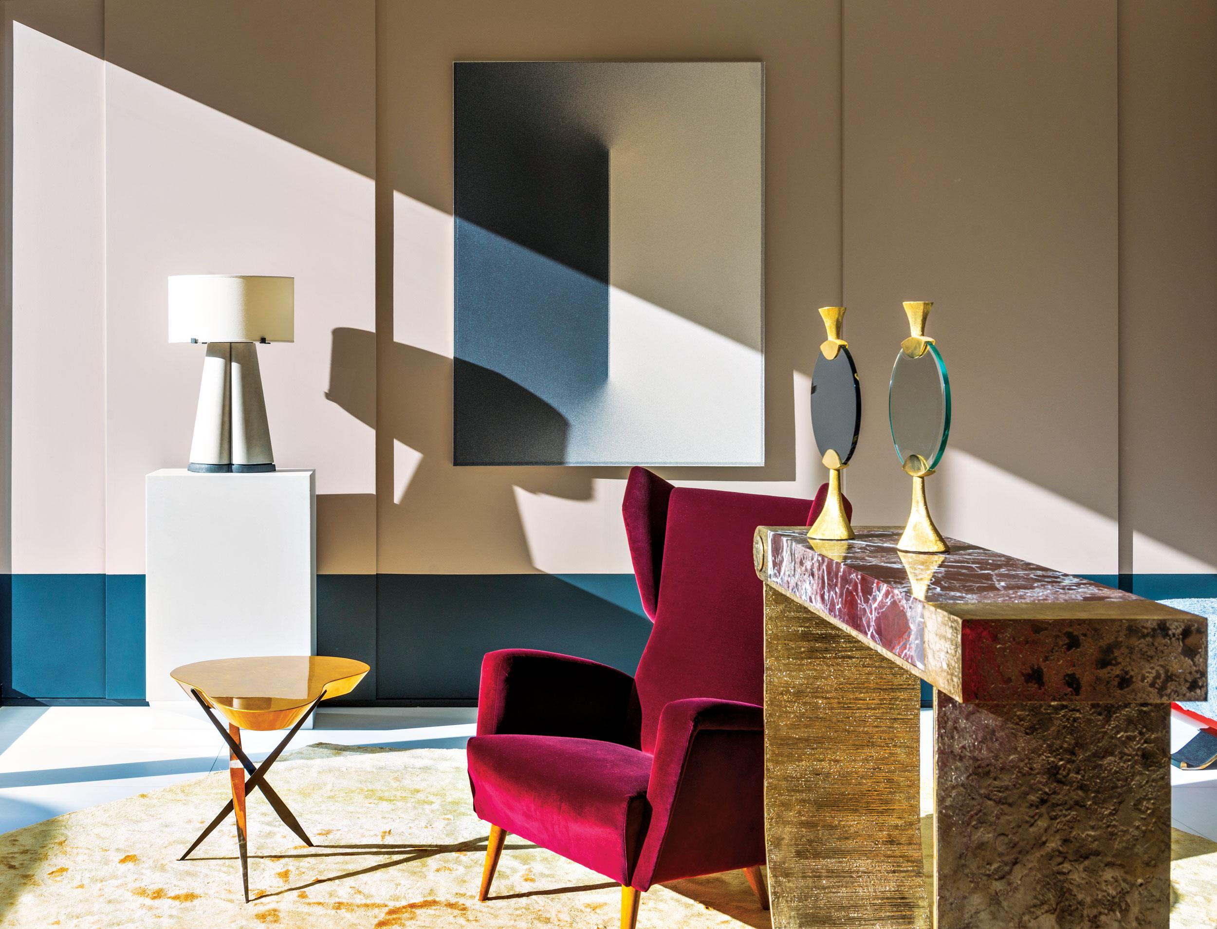 Modern living room with red armchair, marble side table, gold candlesticks, and contemporary art on the wall.