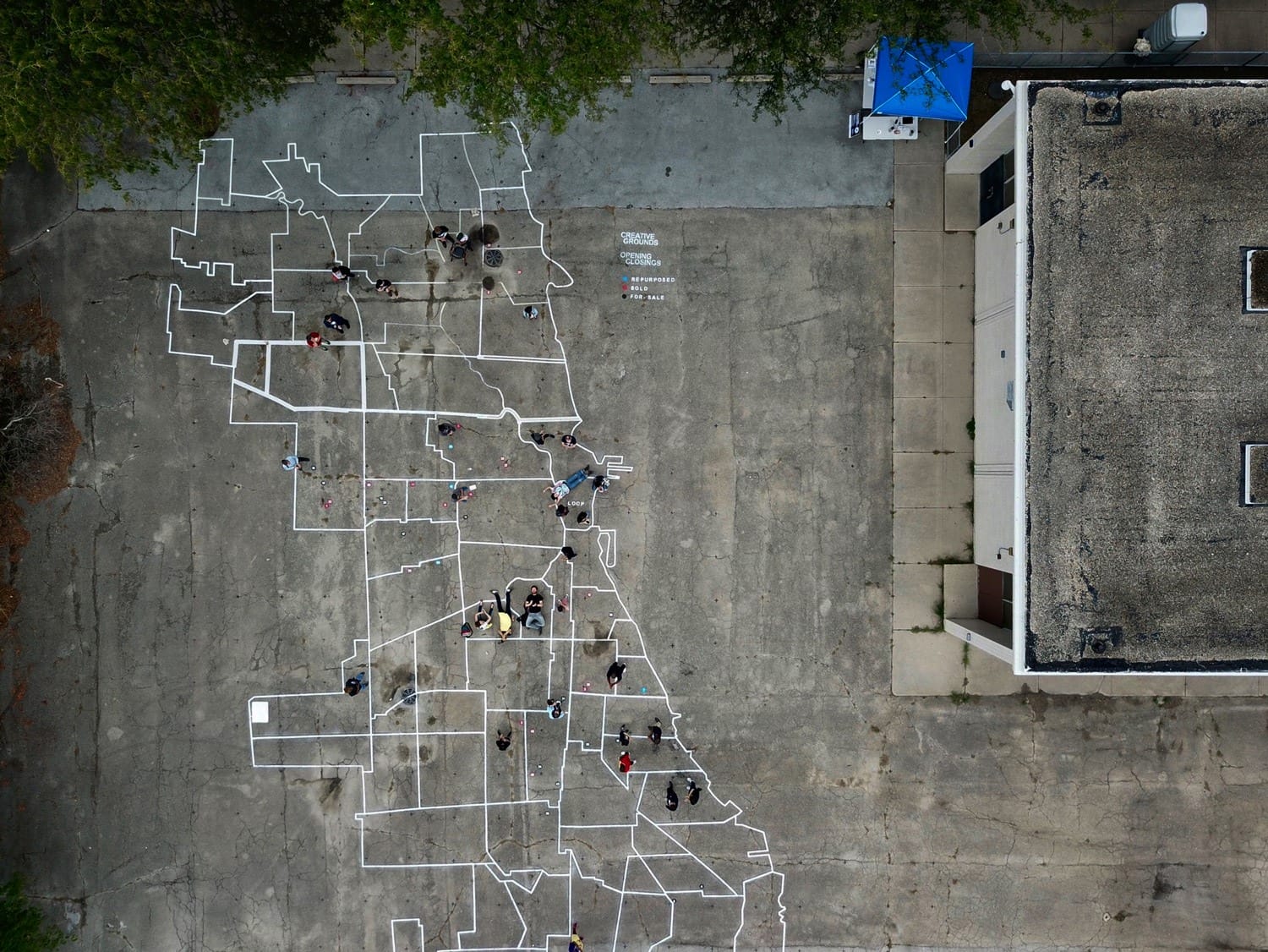 People gathered on a large map drawn on a concrete surface next to a building, photographed from above.