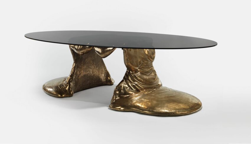 Oval glass top table with unique gold-colored sculptural base resembling draped fabric.