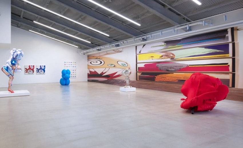 Contemporary art gallery with abstract sculptures and colorful wall murals under industrial overhead lighting.