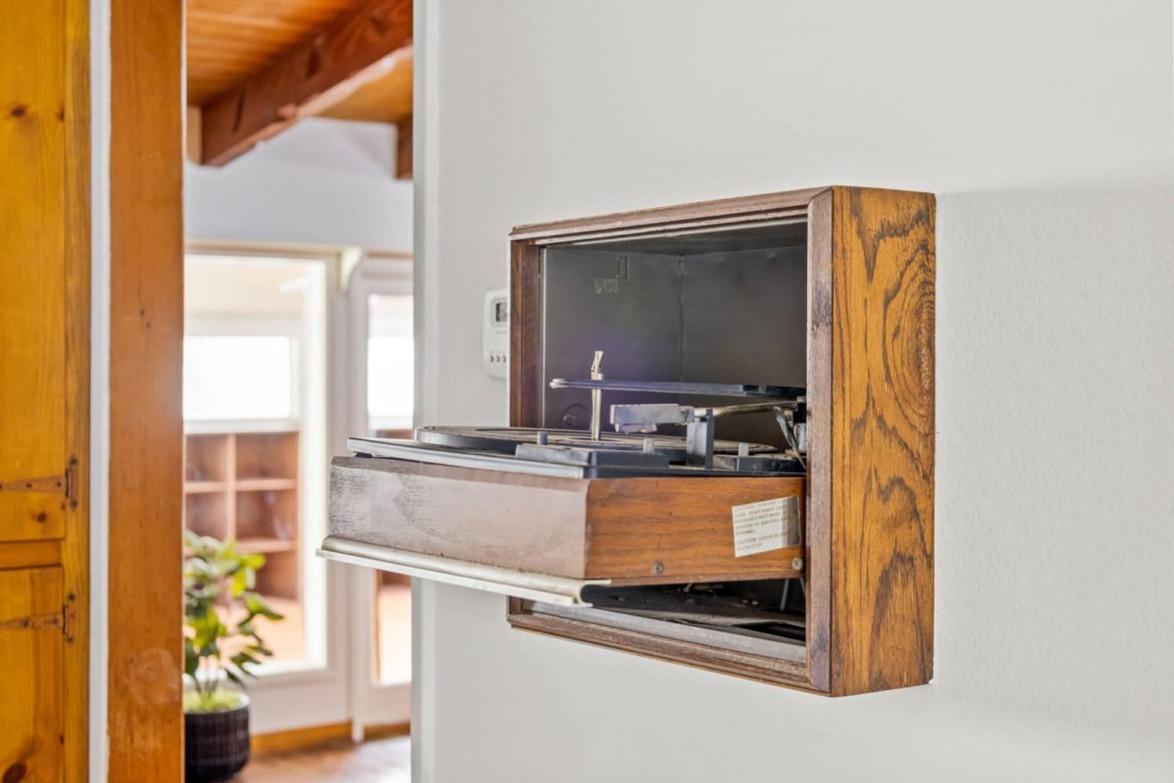 Built-in vintage record player in a wooden enclosure on a white wall, with sunlight streaming through nearby windows.