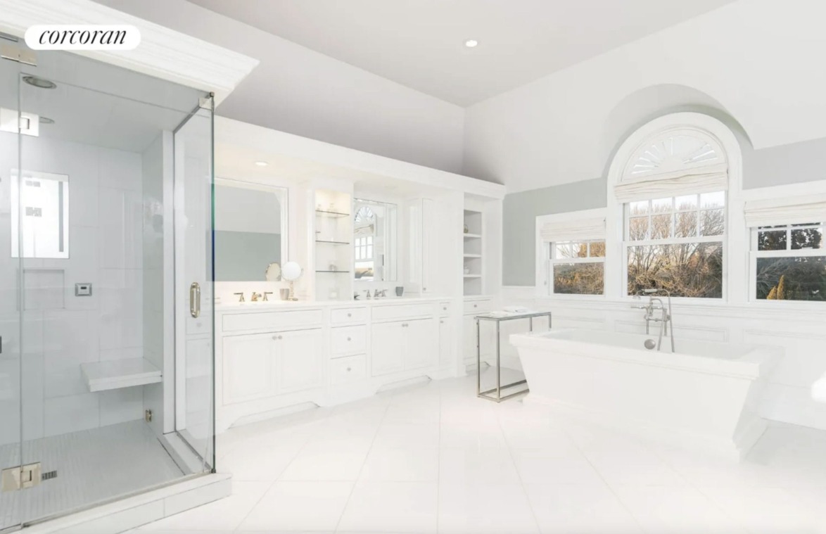 Spacious white bathroom with large bathtub, glass shower, and double vanity featuring natural light from large windows.