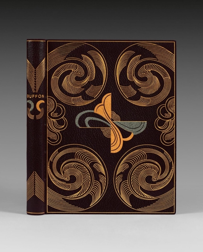 Leather-bound book with intricate swirling patterns and geometric designs in gold and silver on a dark cover.