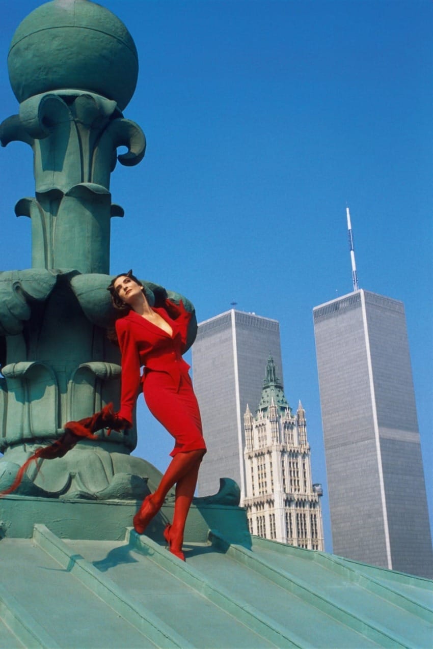 Person in a red outfit poses on a rooftop with iconic skyscrapers and blue sky in the background.