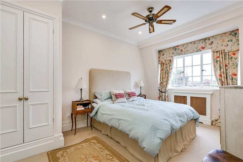 Cozy bedroom with a double bed, floral curtains, a ceiling fan, and bedside lamps, featuring a light and airy decor.