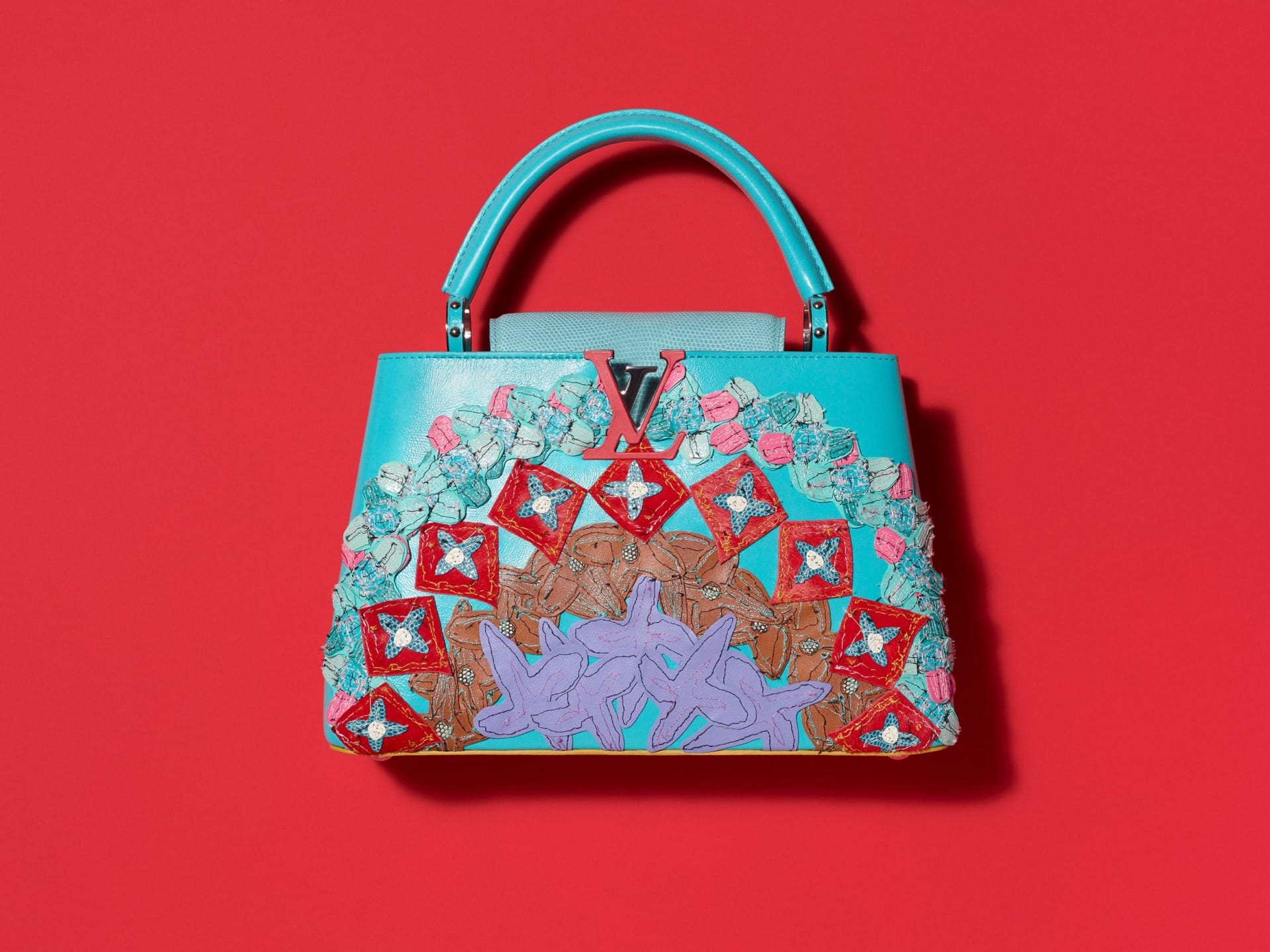 Colorful designer handbag with intricate floral patterns on a vibrant red background