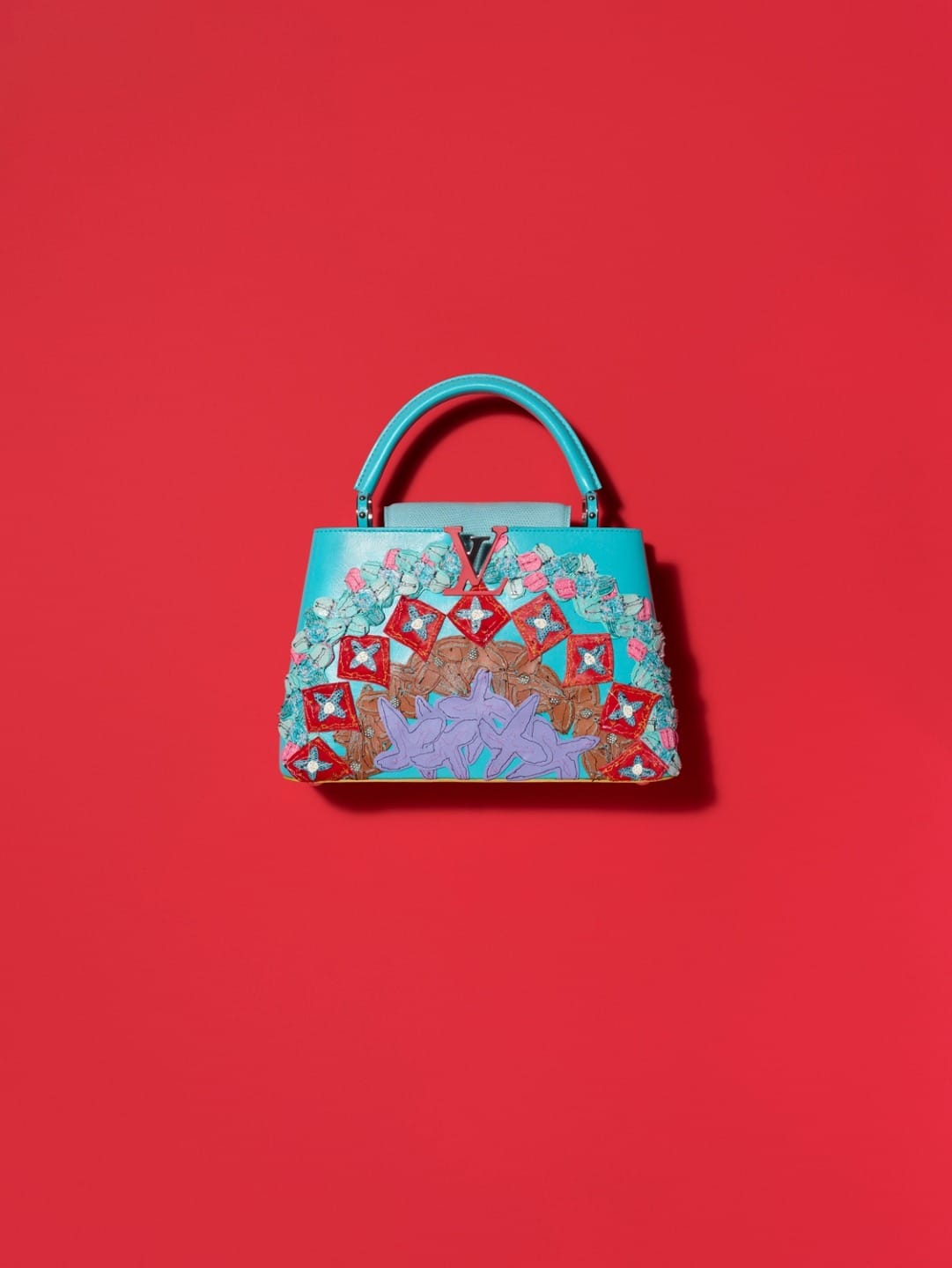 Turquoise handbag with colorful decorative embellishments on a vibrant red background.