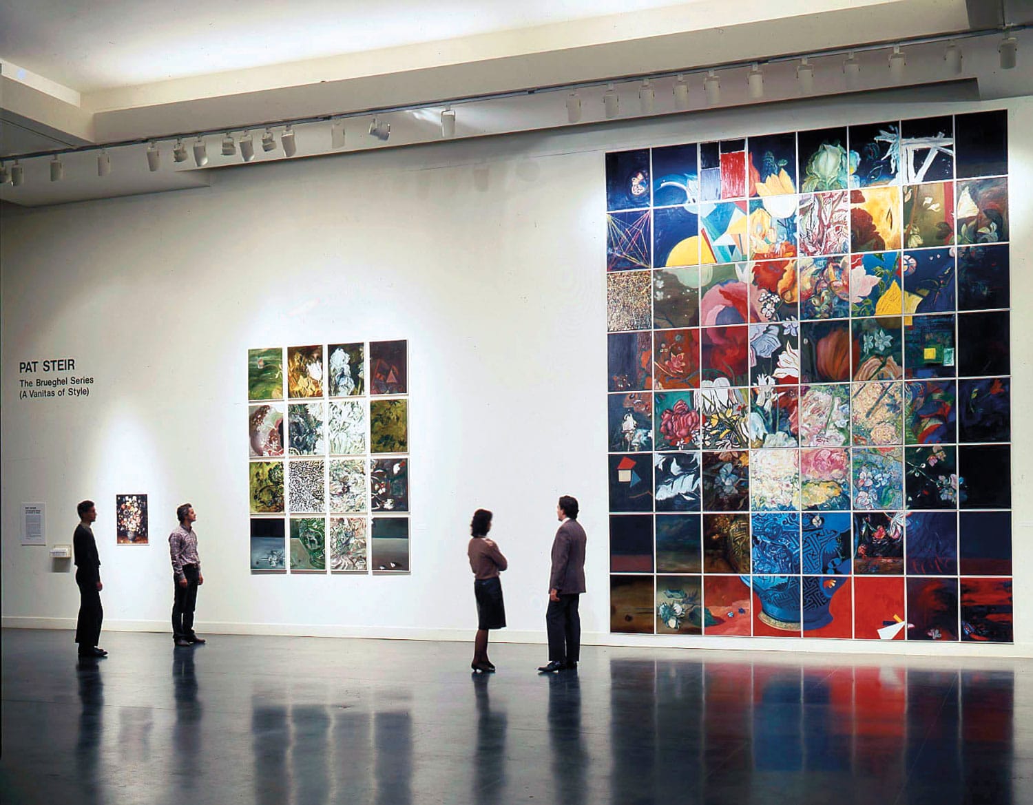 People viewing large, colorful mosaic artwork on a gallery wall.