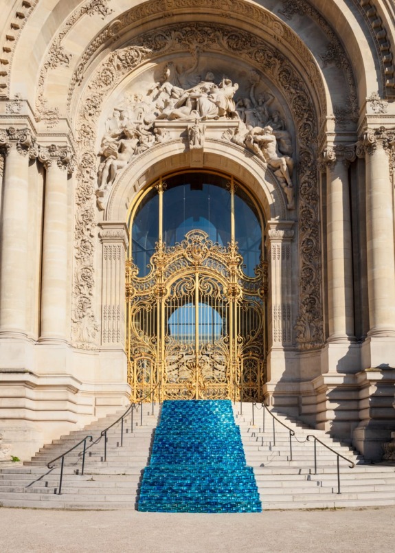 Ornate building entrance with decorative arch, golden gate, and blue art installation on steps.