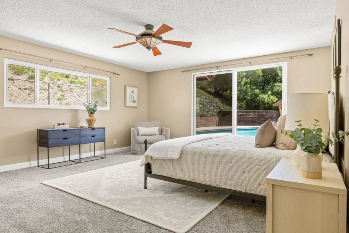 modern bedroom with large windows, view of pool, ceiling fan, neutral tones, cozy armchair, and minimalist furnishings