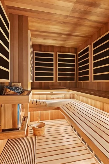 Wooden sauna interior with benches, infrared panels, and a bucket with a ladle on the floor.