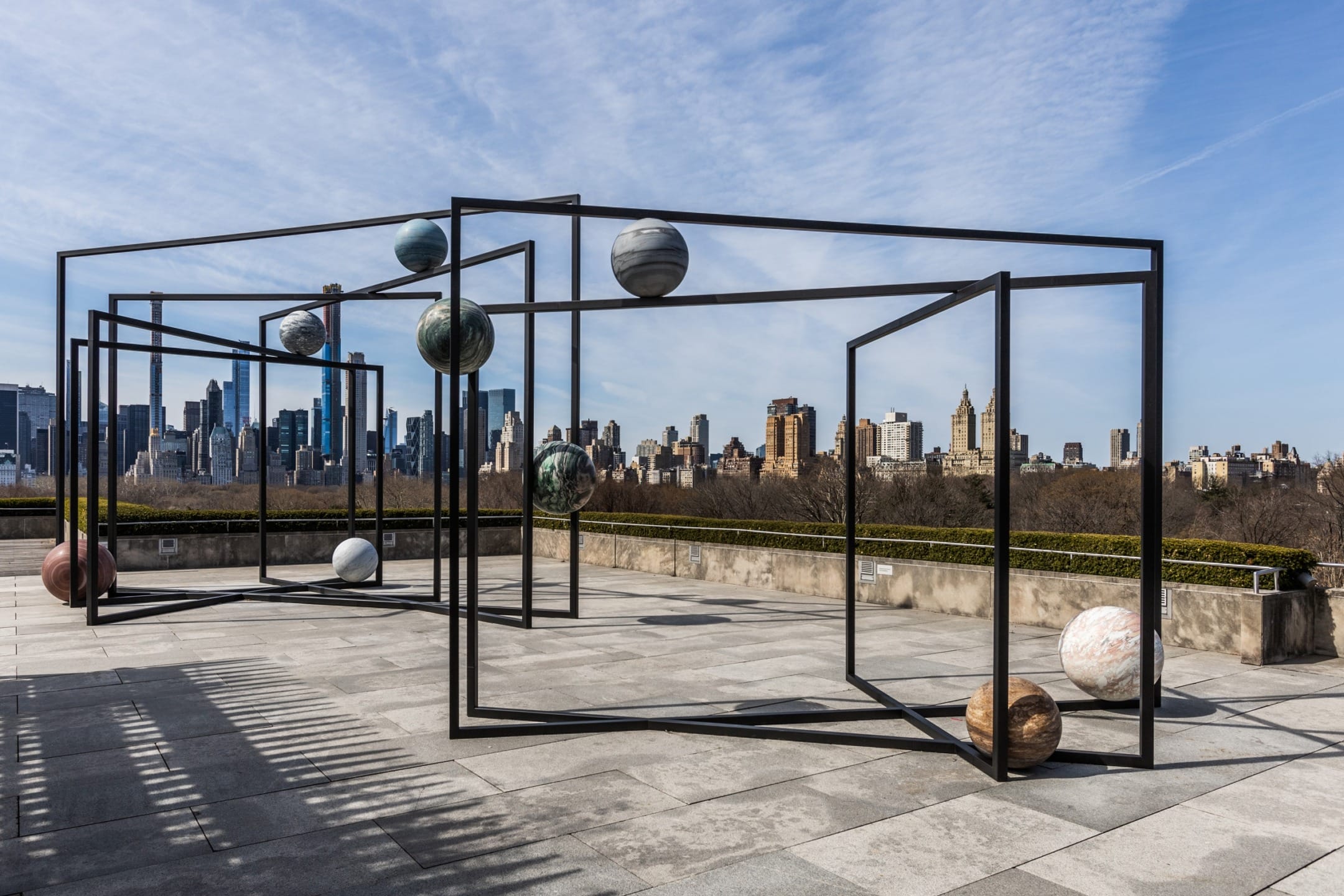 Outdoor modern art installation with geometric frames and stone spheres on a rooftop with a city skyline in the background