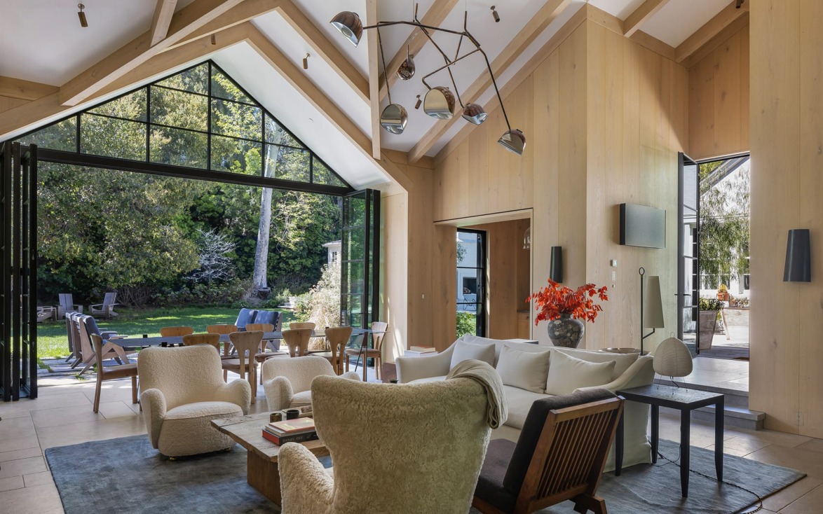 Spacious living room with high ceilings, modern chandelier, and large glass doors opening to a lush garden view.