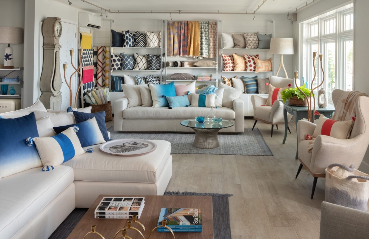 Modern living room with colorful pillows, sofas, a glass coffee table, and shelves showcasing various home decor items.