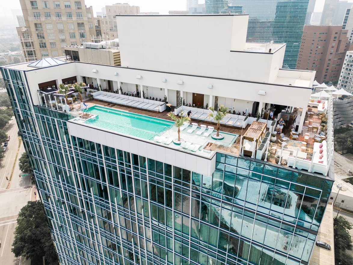 Aerial view of rooftop infinity pool and lounge area on a modern city high-rise building with surrounding cityscape.