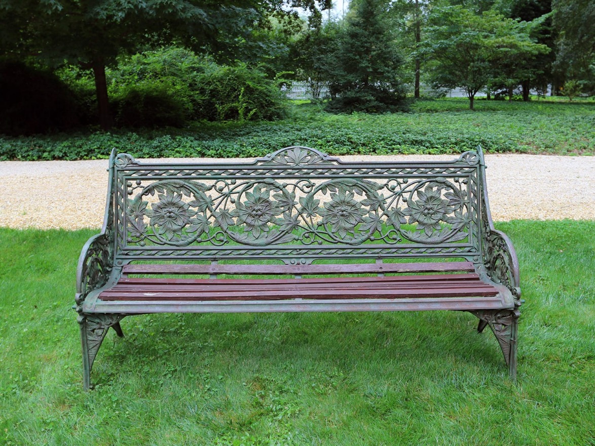 Ornate metal bench with floral design set on a lush green lawn in a garden setting.