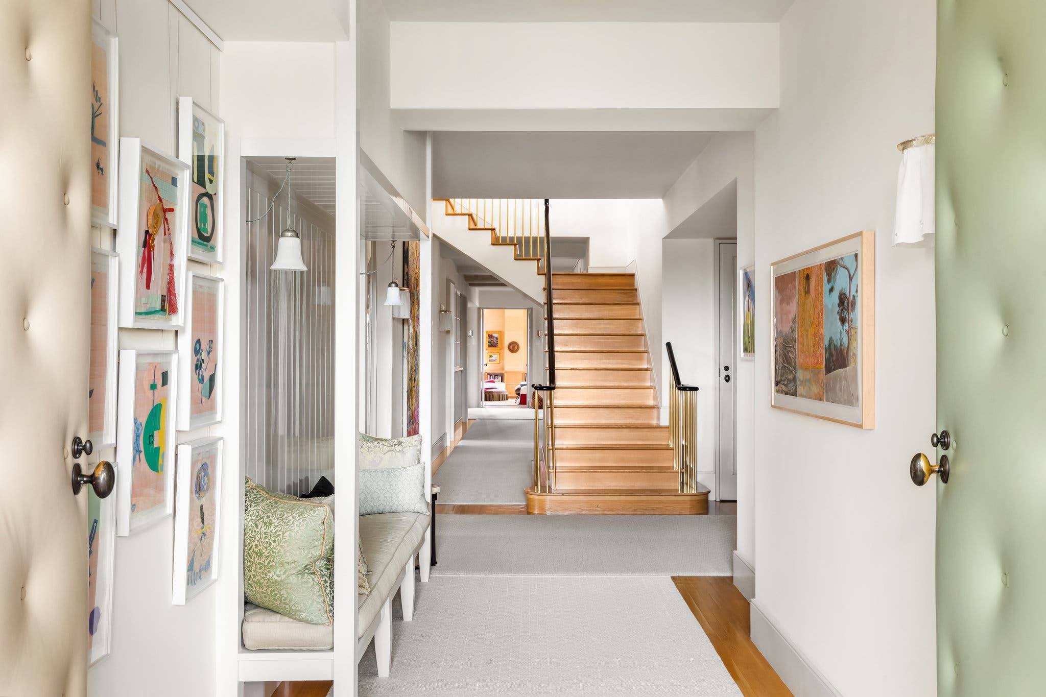 Spacious modern hallway with wooden staircase, art on walls, bench seating, and soft neutral tones.