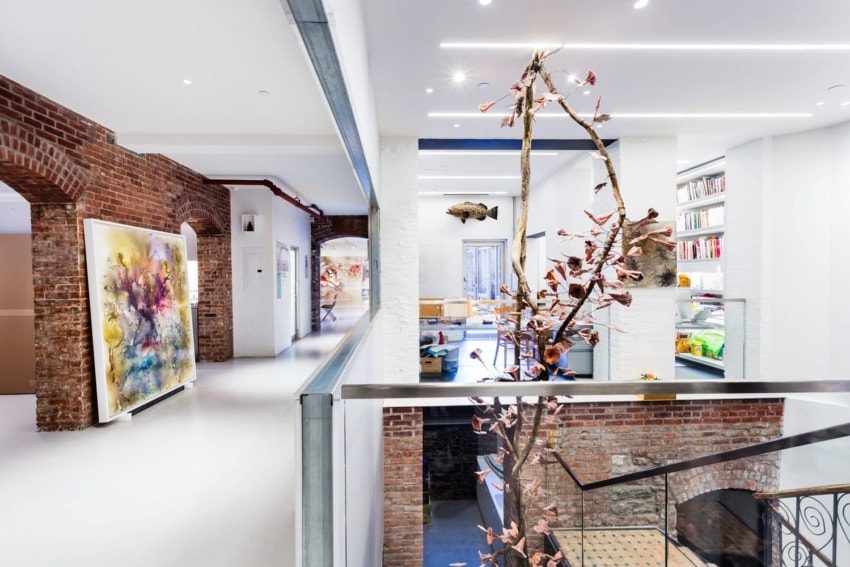 Open-concept loft office with exposed brick walls, modern artwork, and contemporary furniture, featuring a central staircase.