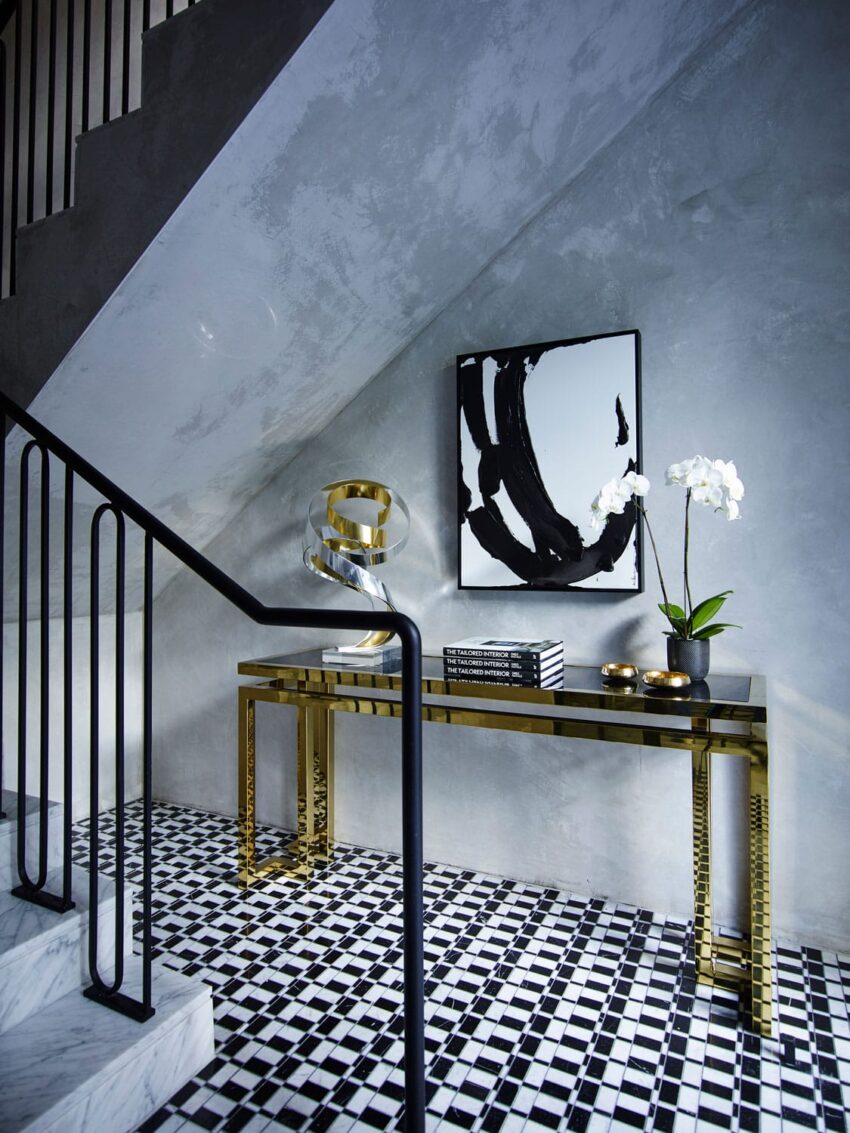 Modern hallway with black and white decor, gold accent table, abstract art, and a potted orchid under a staircase.