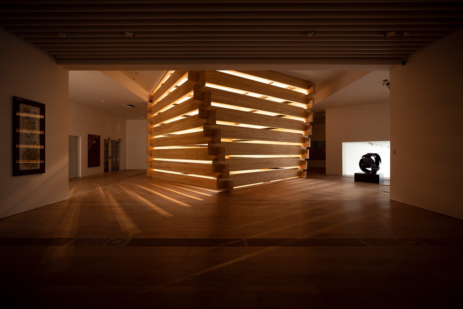 Dimly lit, modern art installation with wooden structure and ambient lighting in a spacious gallery.