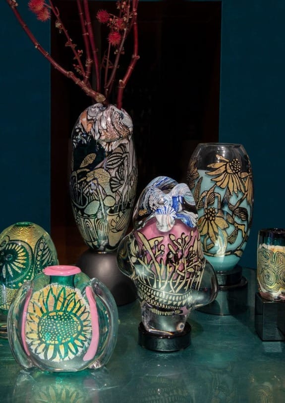 Colorful glass vases with intricate floral designs on display against a teal background.