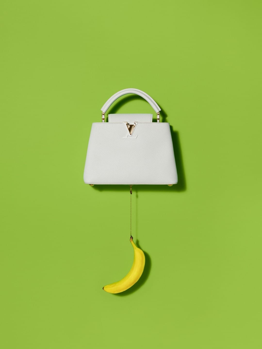 White handbag hanging with a banana on a bright green background