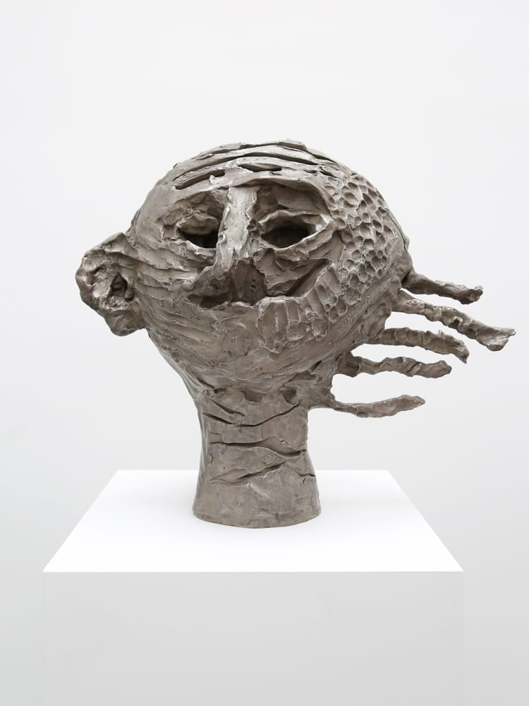 Abstract sculpture of a human head with exaggerated features on a pedestal, featuring a textured surface and unique design.