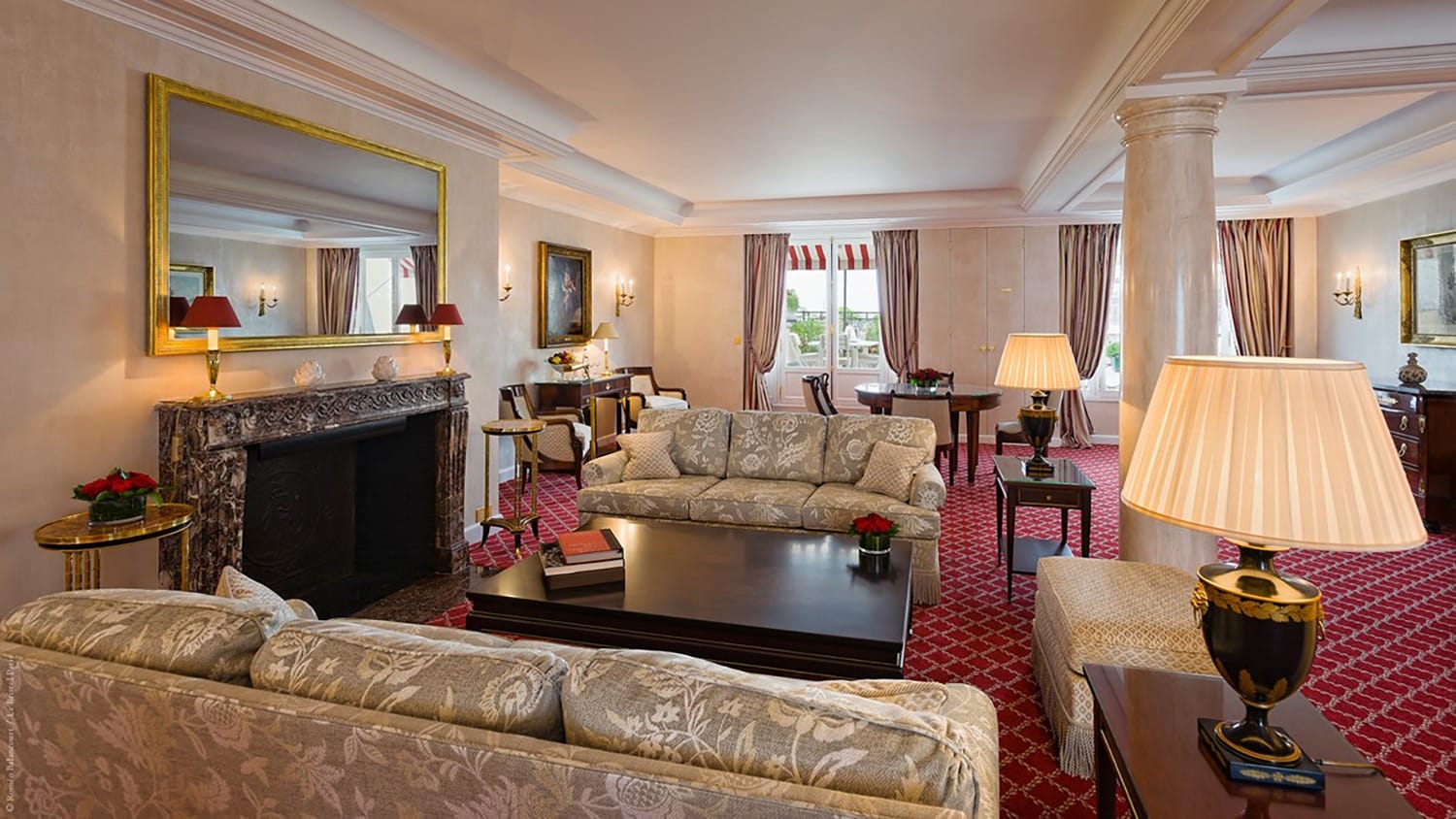 Luxurious hotel suite with elegant furniture, large mirrors, and ornate decor in a spacious living area with red carpet.