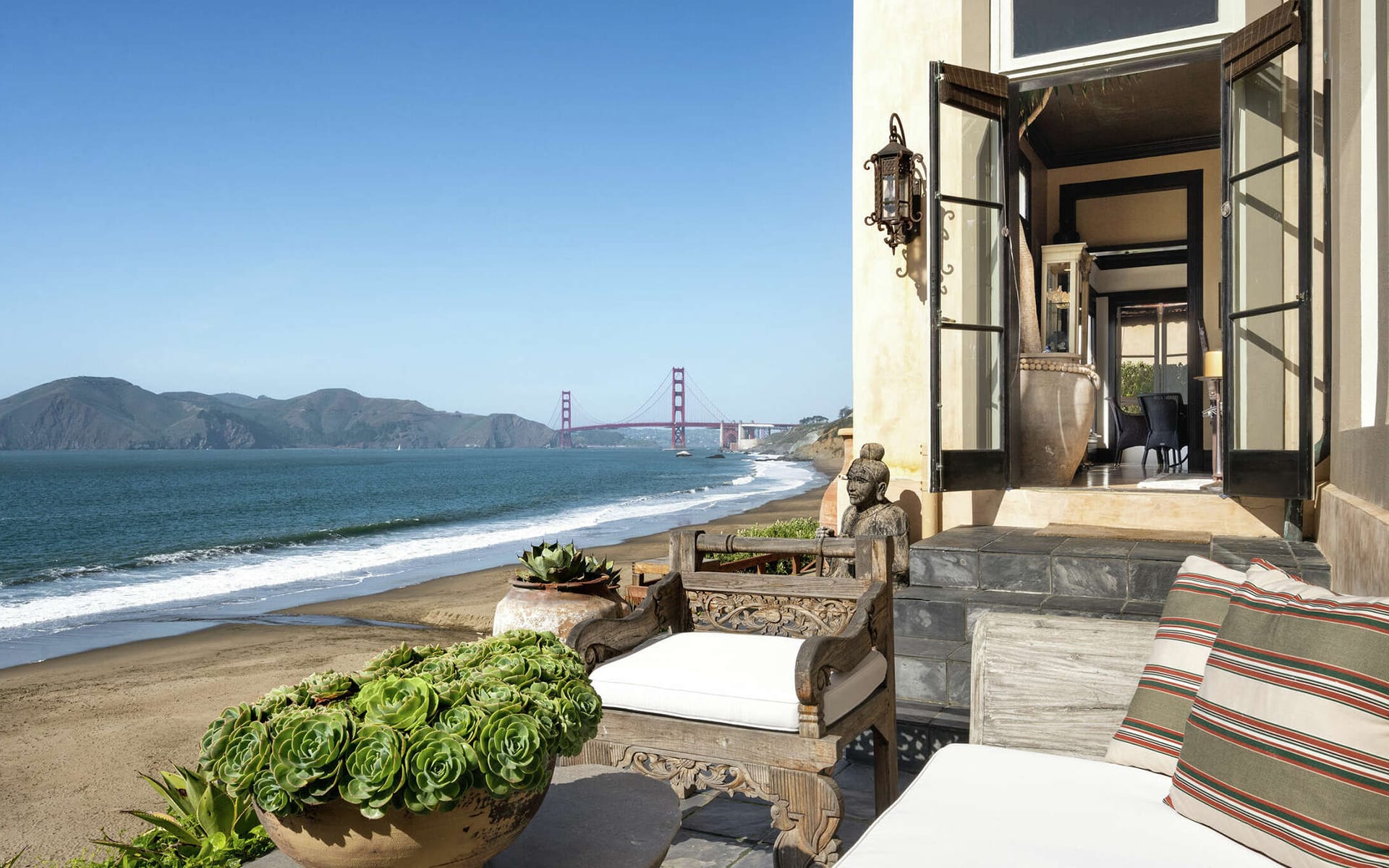 Beachfront patio with succulent plants, overlooking ocean and Golden Gate Bridge in the distance on a clear day.