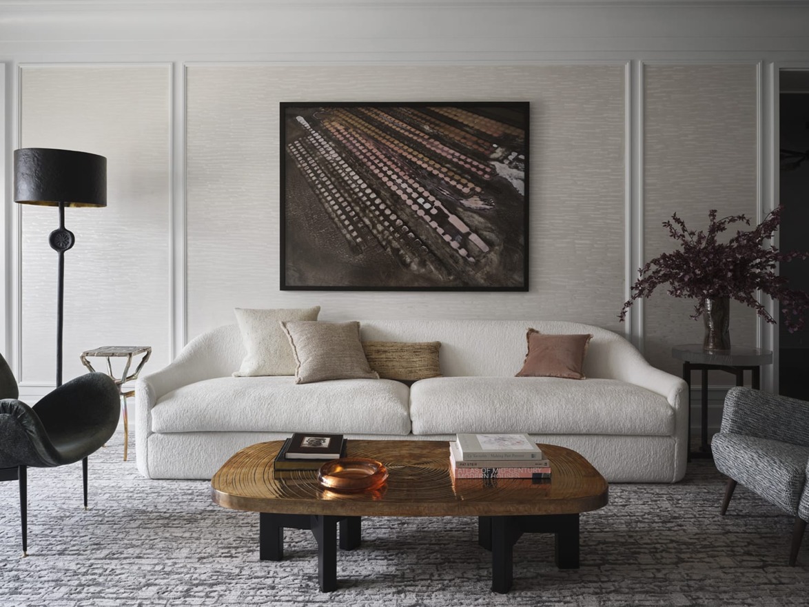 Modern living room with white sofa, patterned rug, wooden coffee table, and wall art in a neutral-toned decor setting.