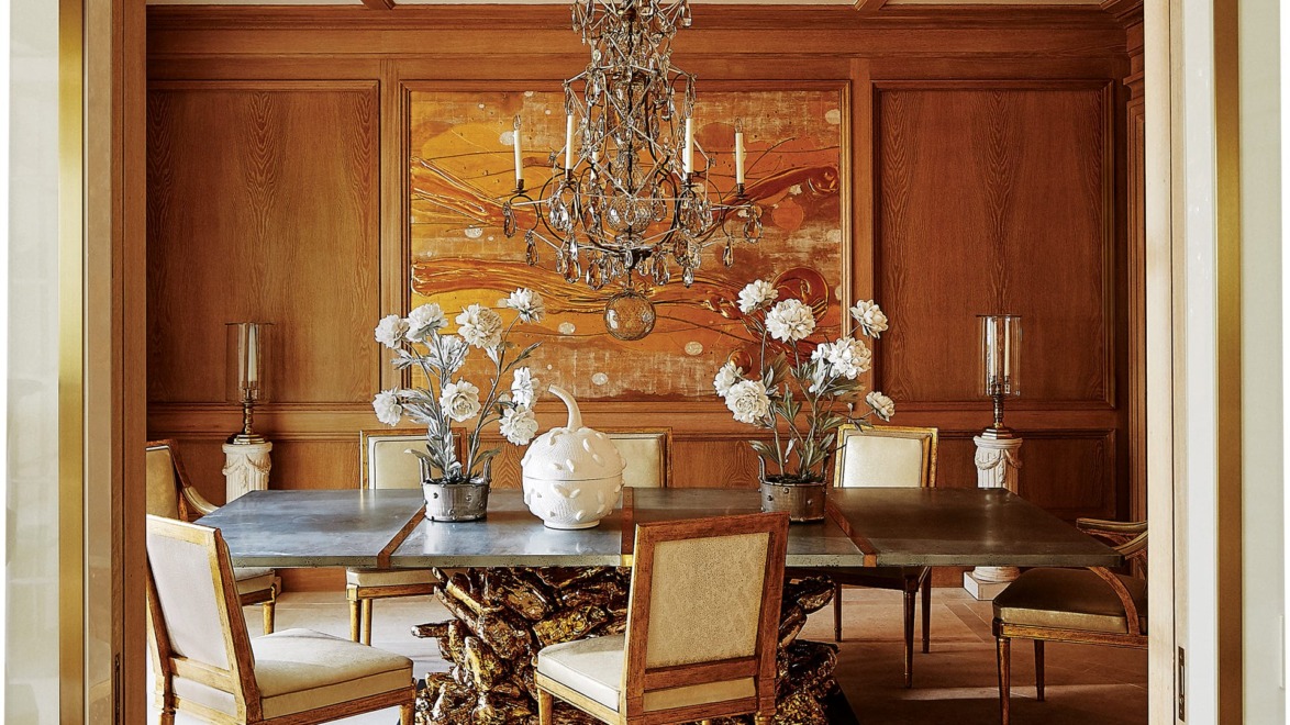Elegant dining room with chandelier, modern art, and wooden table surrounded by upholstered chairs and decorative vases.