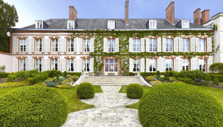 Large historic mansion with ivy-covered facade, white-framed windows, and manicured garden in the foreground.
