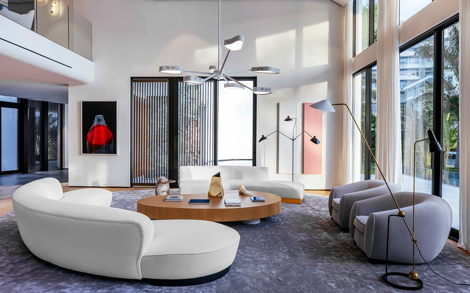 Modern living room with white sofas, large windows, abstract art, and a central wooden coffee table.