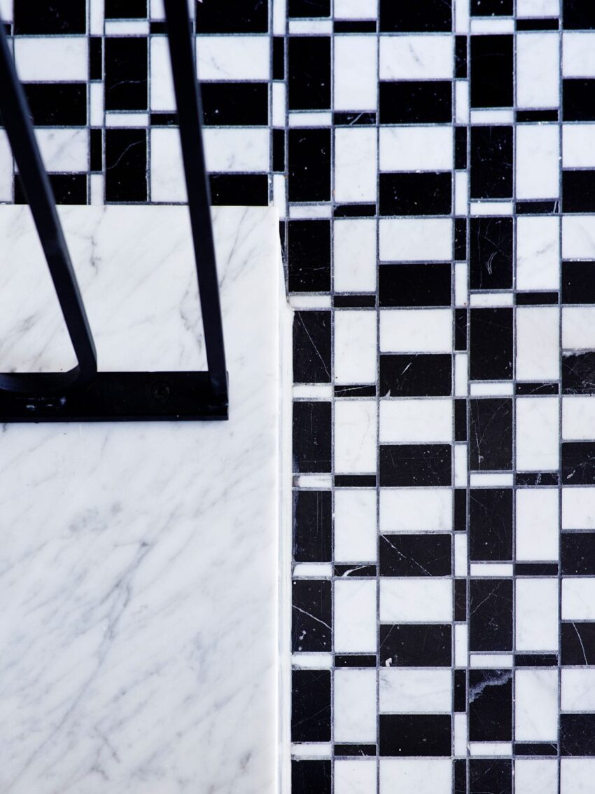 Black and white geometric tiled floor next to a marble surface with a black metal railing.