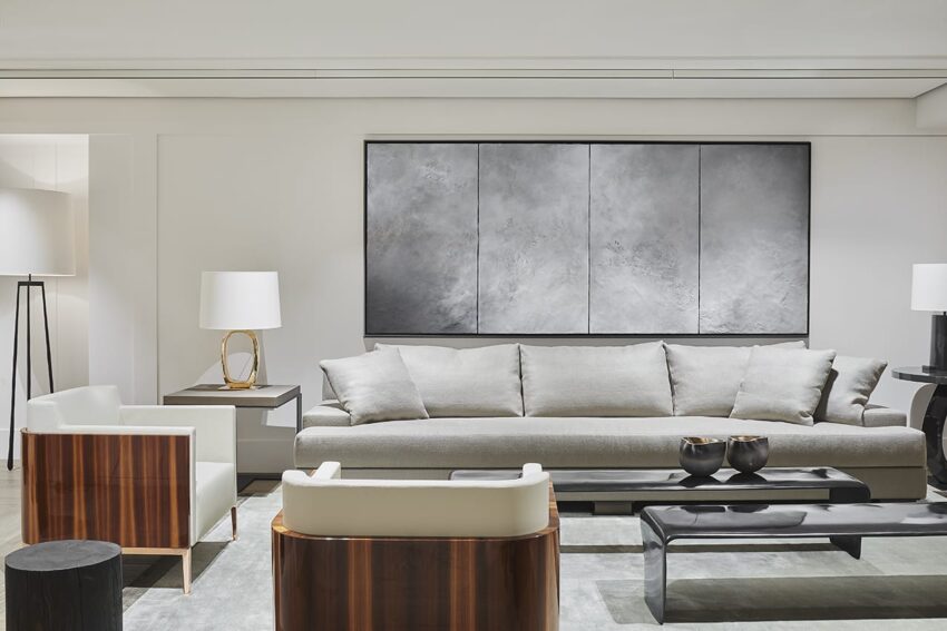 Modern living room with a large gray sofa, contemporary art on the wall, wooden armchairs, and stylish lighting.