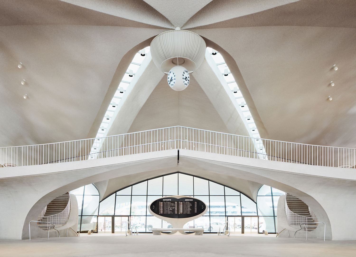 Interior of a modern architectural building with high arched ceilings, large clock, and central seating area.