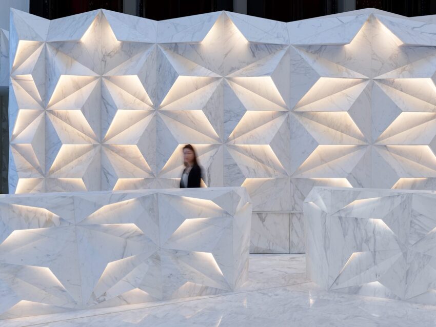 Person walking past a modern geometric marble wall with illuminated triangular patterns in a minimalist architectural setting.