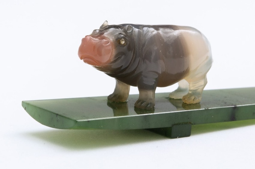 Carved stone figure of a hippopotamus on a green base, showcasing detailed craftsmanship against a plain background.