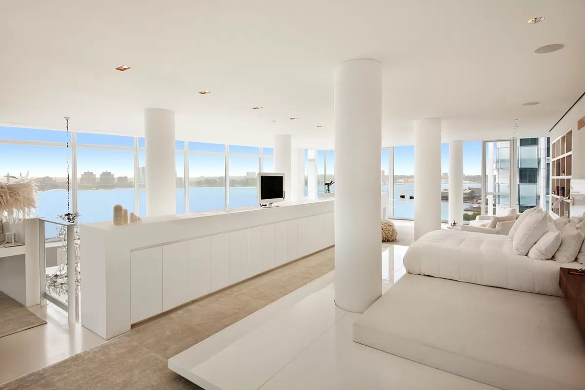 Spacious modern living room with white furnishings and large windows offering a scenic view of a body of water.