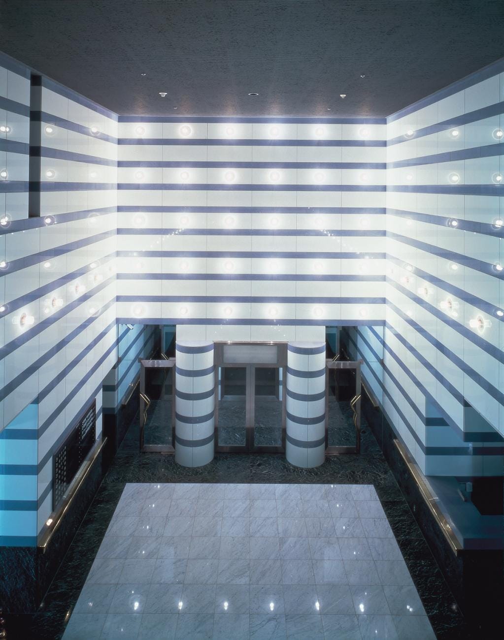 Brightly lit modern lobby with striped walls, circular glass entrance, and marble floor.