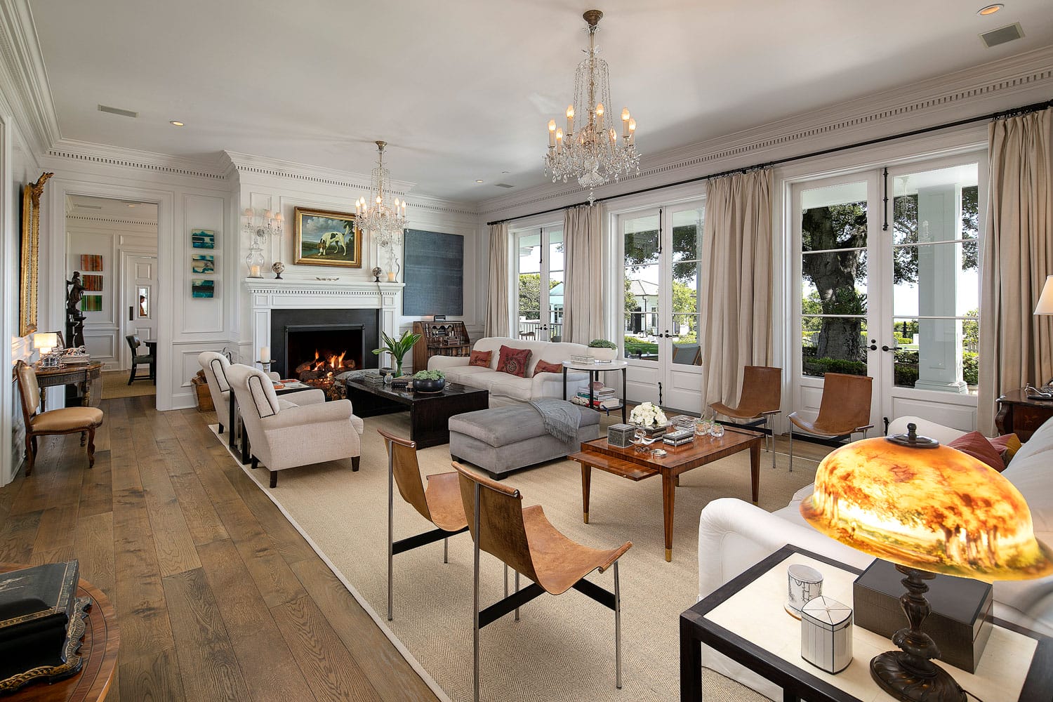 Luxurious living room interior with elegant furnishings, chandelier, fireplace, large windows, and wooden floor.