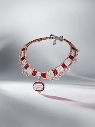 Elegant diamond and ruby necklace with intricate design and central pendant resting on a soft, blurred background.