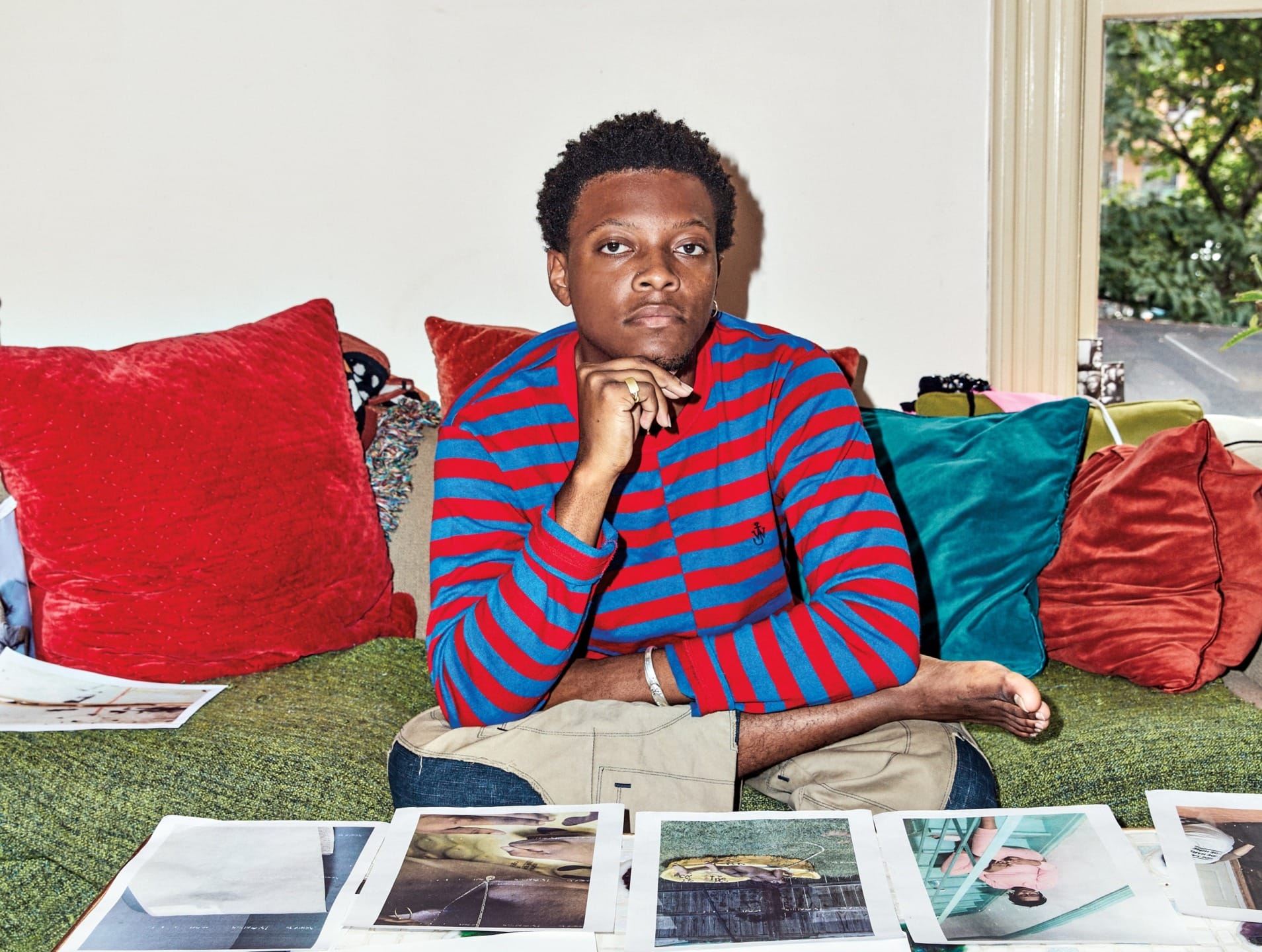 Person in a striped shirt sitting on a green sofa with colorful pillows, looking thoughtful, with photos in front.