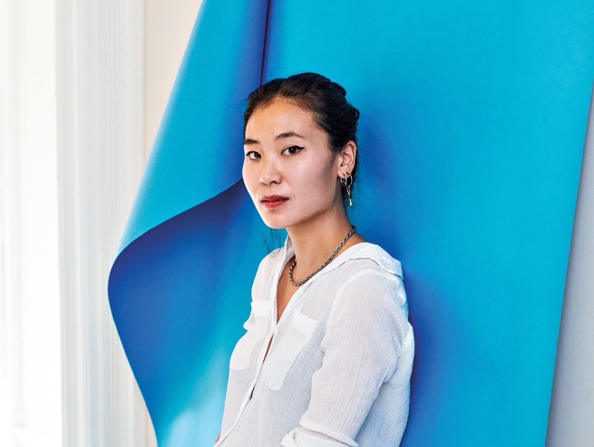 Woman in white shirt standing against a blue abstract background, looking at the camera.